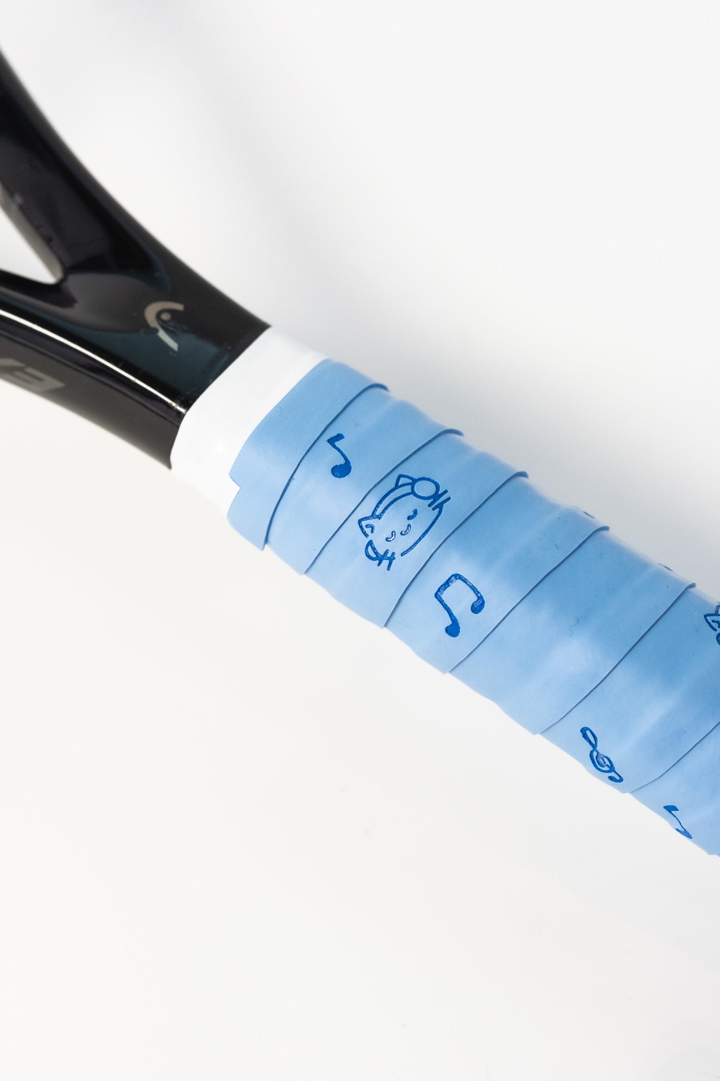 Close-up of blue cat and music note tennis overgrip securely wrapped on racket.