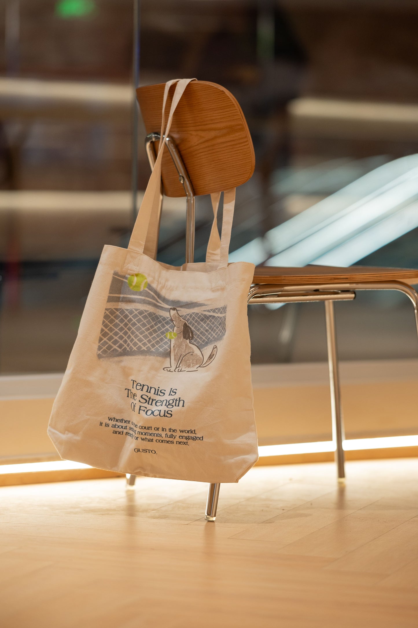 Blue tennis canvas tote bag with focused dog illustration, hanging on a chair