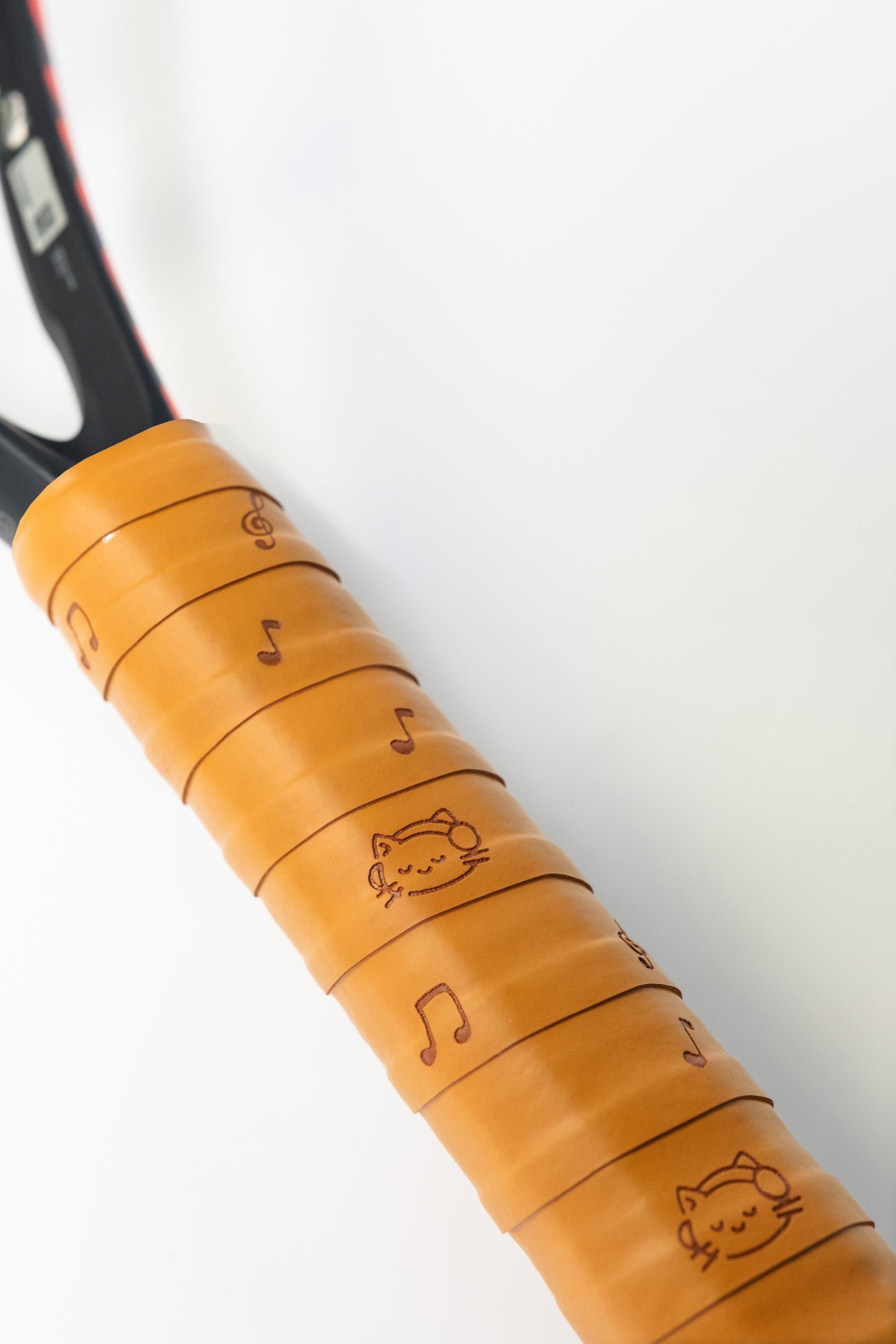 Durable brown tennis grip featuring cat and music note motif, wrapped for secure hold.