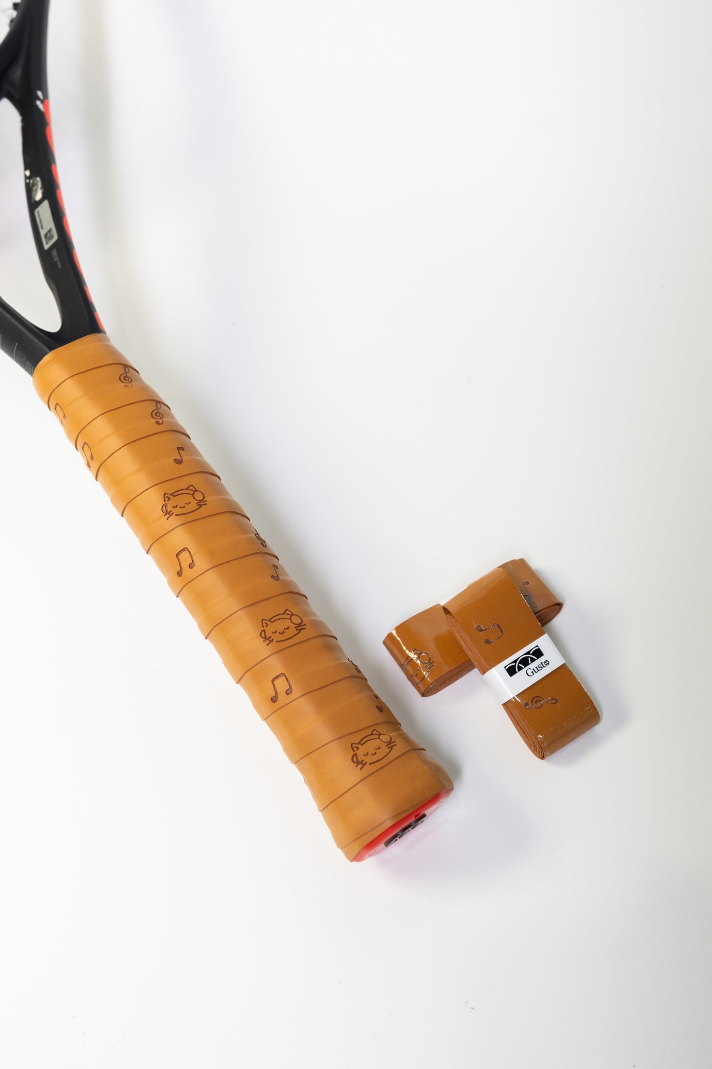 Brown sticky PU grip tape with cat and music note design, fitted on racket handle.