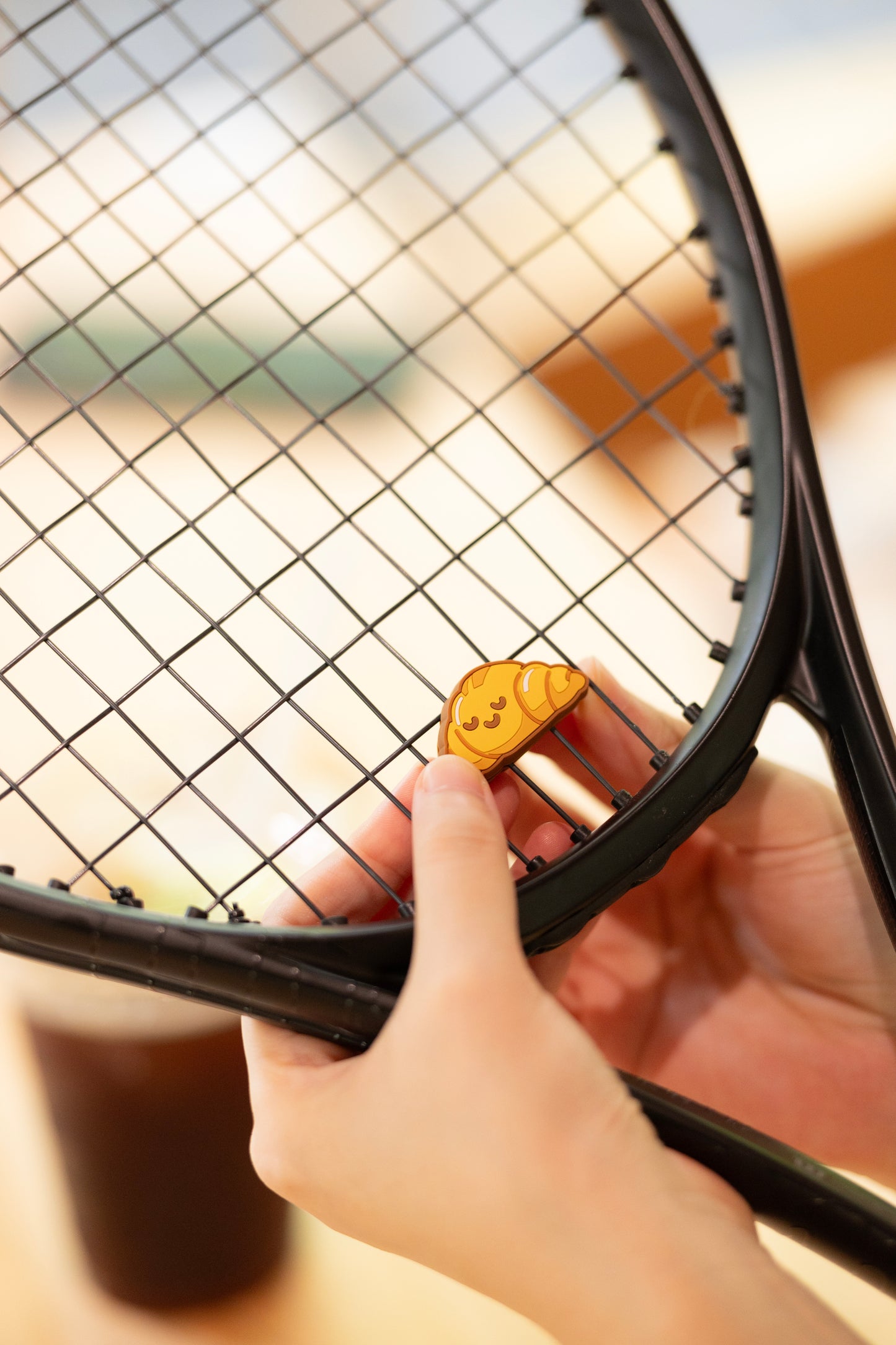 odel installing croissant shaped tennis vibration dampener on racket strings, bakery series tennis accessory