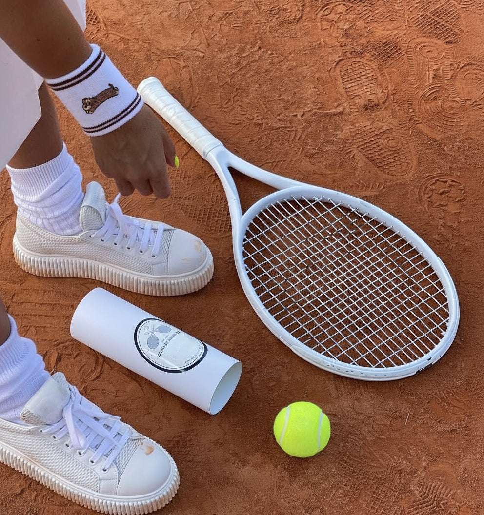 Model playing tennis while wearing white cotton sports wristband with dachshund embroidery
