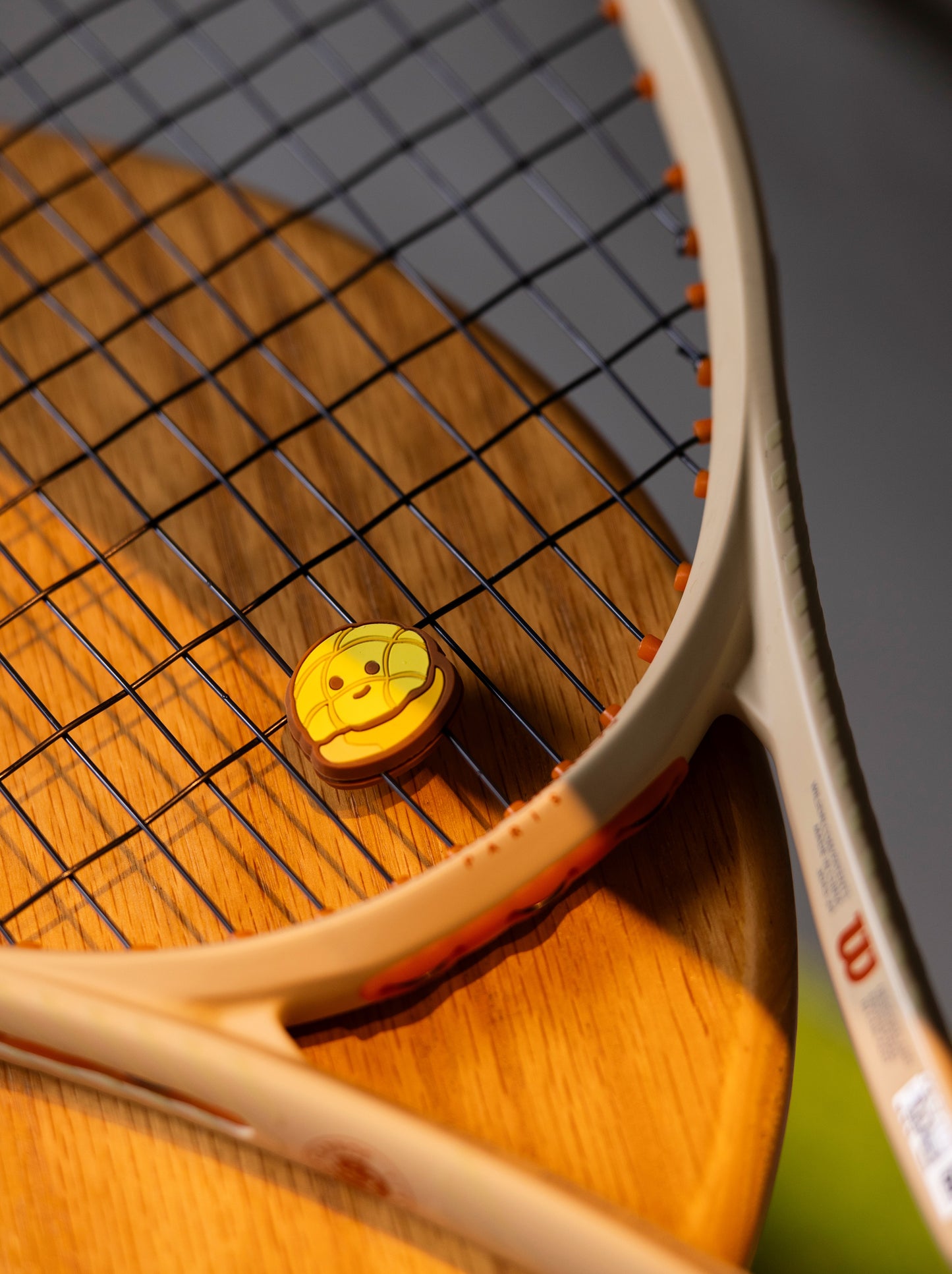Pineapple bun shaped tennis racket dampener photographed in café lifestyle setting, bakery series accessory