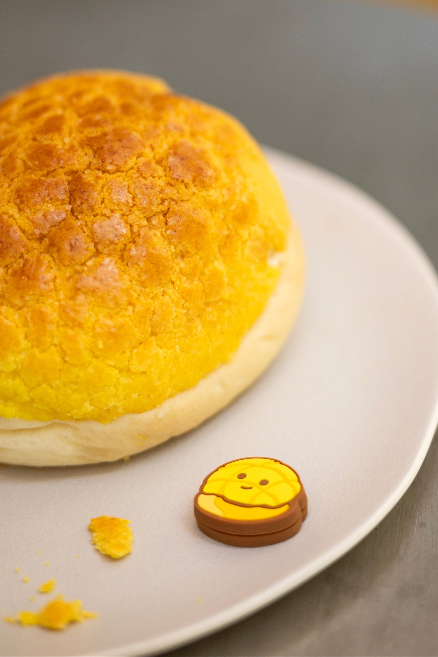 Fun photo of pineapple bun shaped tennis vibration dampener placed on real pineapple bun bread
