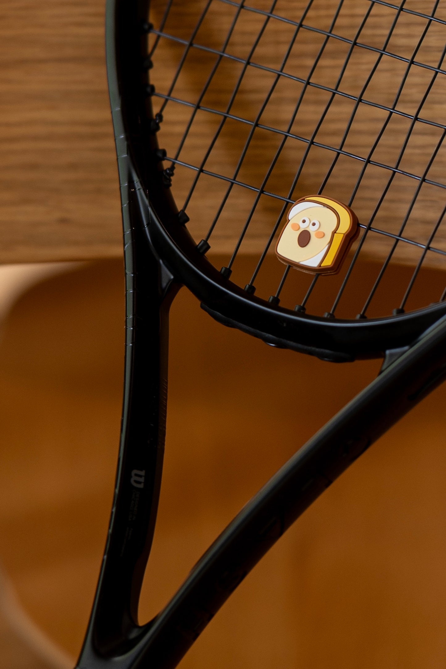 Toast tennis dampener placed on black tennis racket strings, bakery series vibration absorber