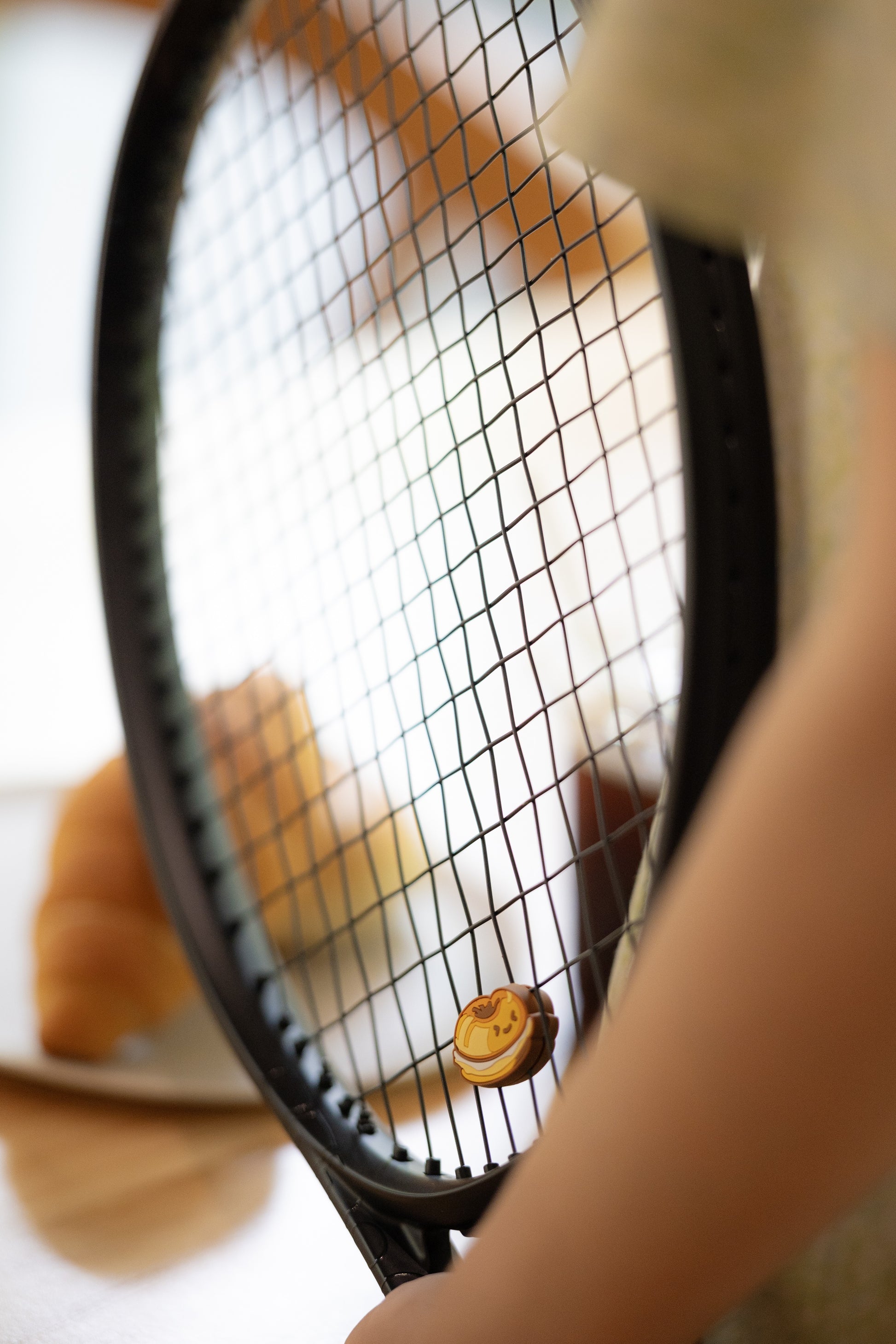 Bagel shaped tennis vibration dampener photographed in a café lifestyle setting, bakery series tennis accessory
