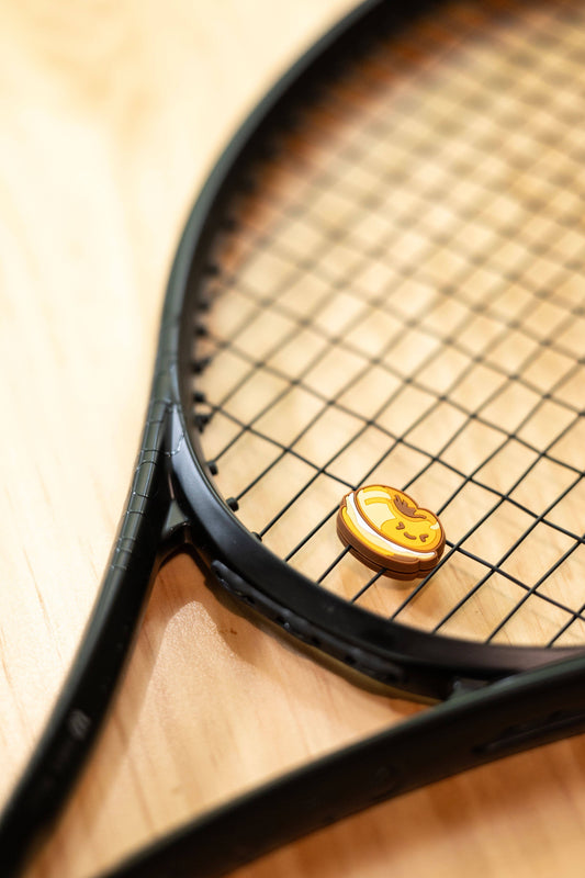 Bagel shaped tennis vibration dampener placed on black racket strings, bakery series design