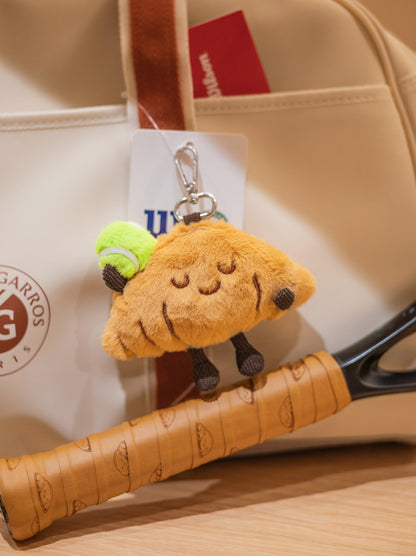 Croissant plush toy with tennis racket and professional tennis bag in product photo