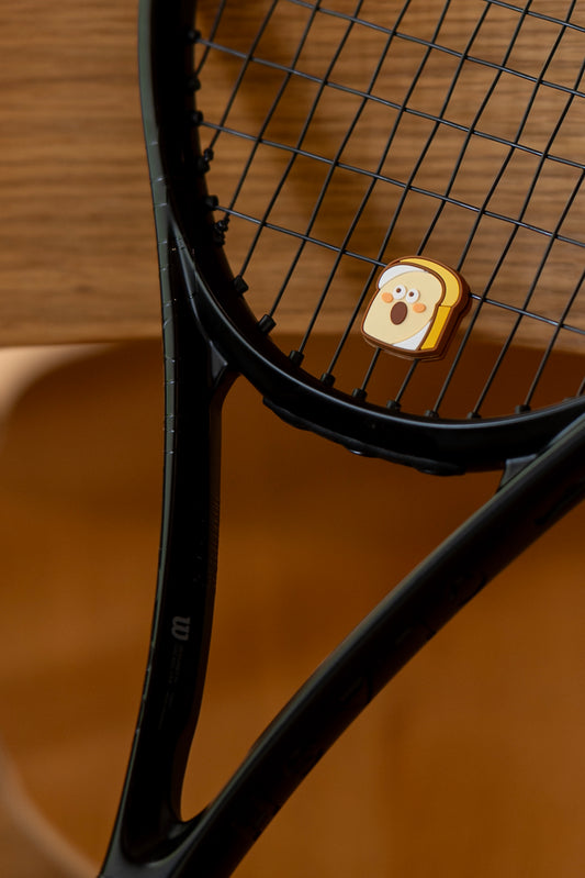 Toast tennis dampener placed on black tennis racket strings, bakery series vibration absorber